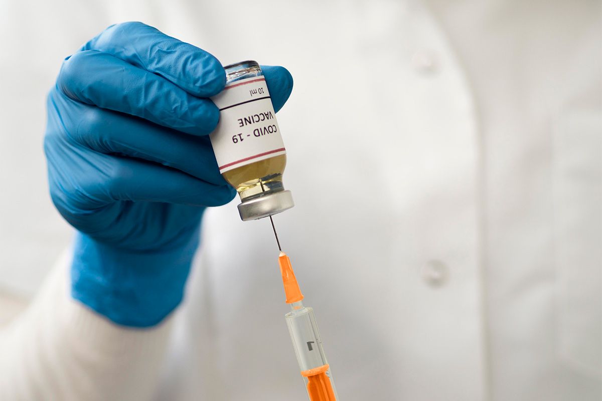 Ein/e Mediziner/in zieht einen Impfstoff für Covid-19 mit der Spritze aus einem Fläschchen.