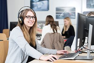 Das Bild zeigt eine junge Frau, die an einem Computer sitzt.