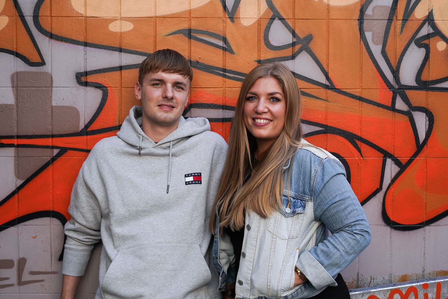 Das Bild zeigt zwei junge Erwachsene vor einer Graffitiwand.
