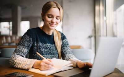 MINT-Praxisbeispiele: MINToring- Studienorientierung praxisnah und individuell. Dieses Foto zeigt eine junge blonde Frau vor einem Laptop, die gerade sich etwas in ihrem Notizbuch notiert.