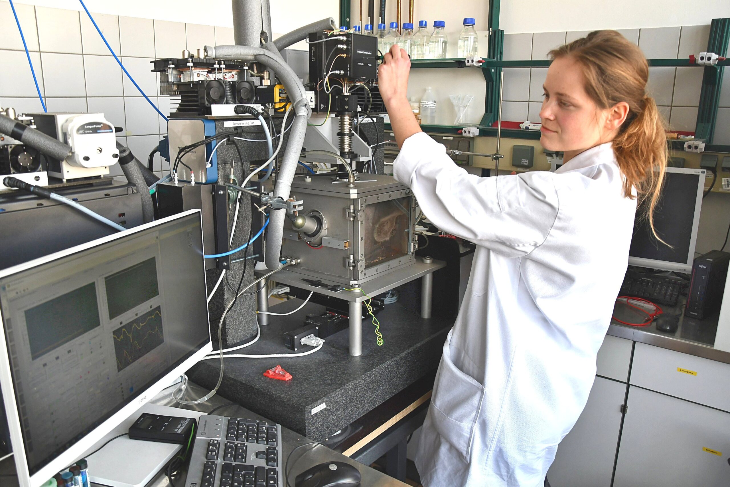 Junge Frau in Labor Kittel bedient eine technische Maschine.