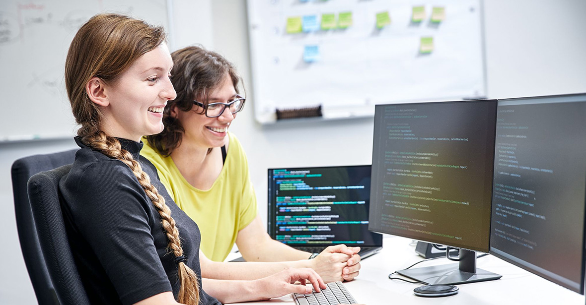 Zwei junge Frauen vor Bildschirmen, die programmieren.