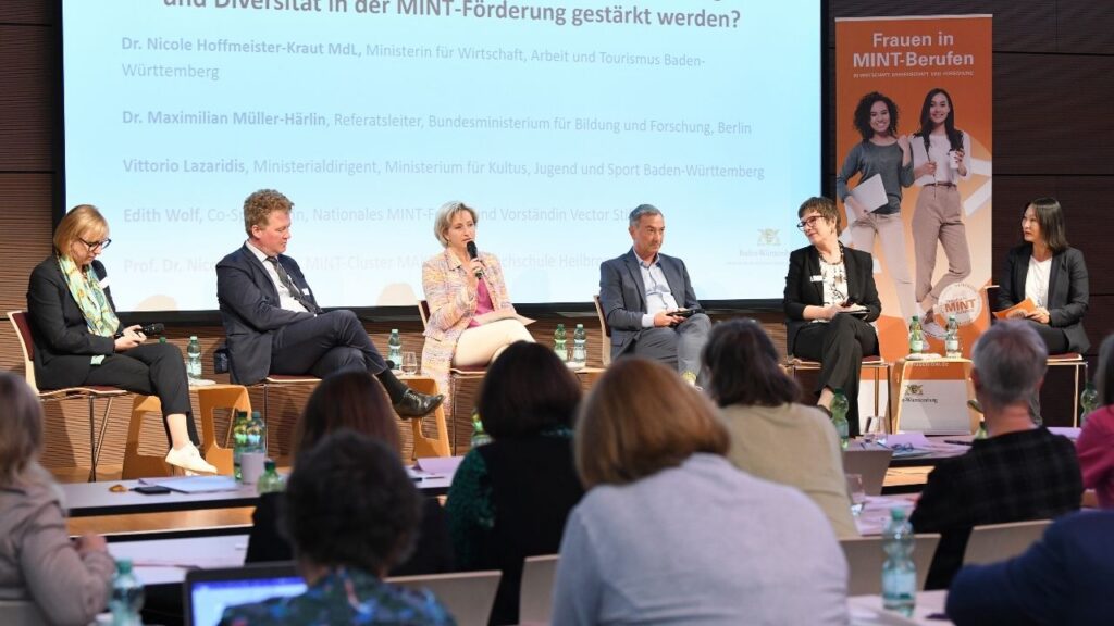 Design ohne Titel (7) Vier Frauen und zwei Männer auf einer Bühne in einem Panel-Talk.