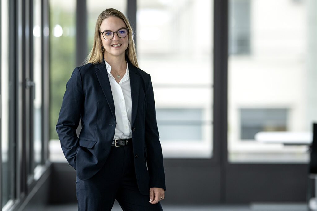 mint_portreat_soraya schwin Eine junge Frau in einem schwarzen Blazer steht vor einem Fenster und lächelt in die Kamera